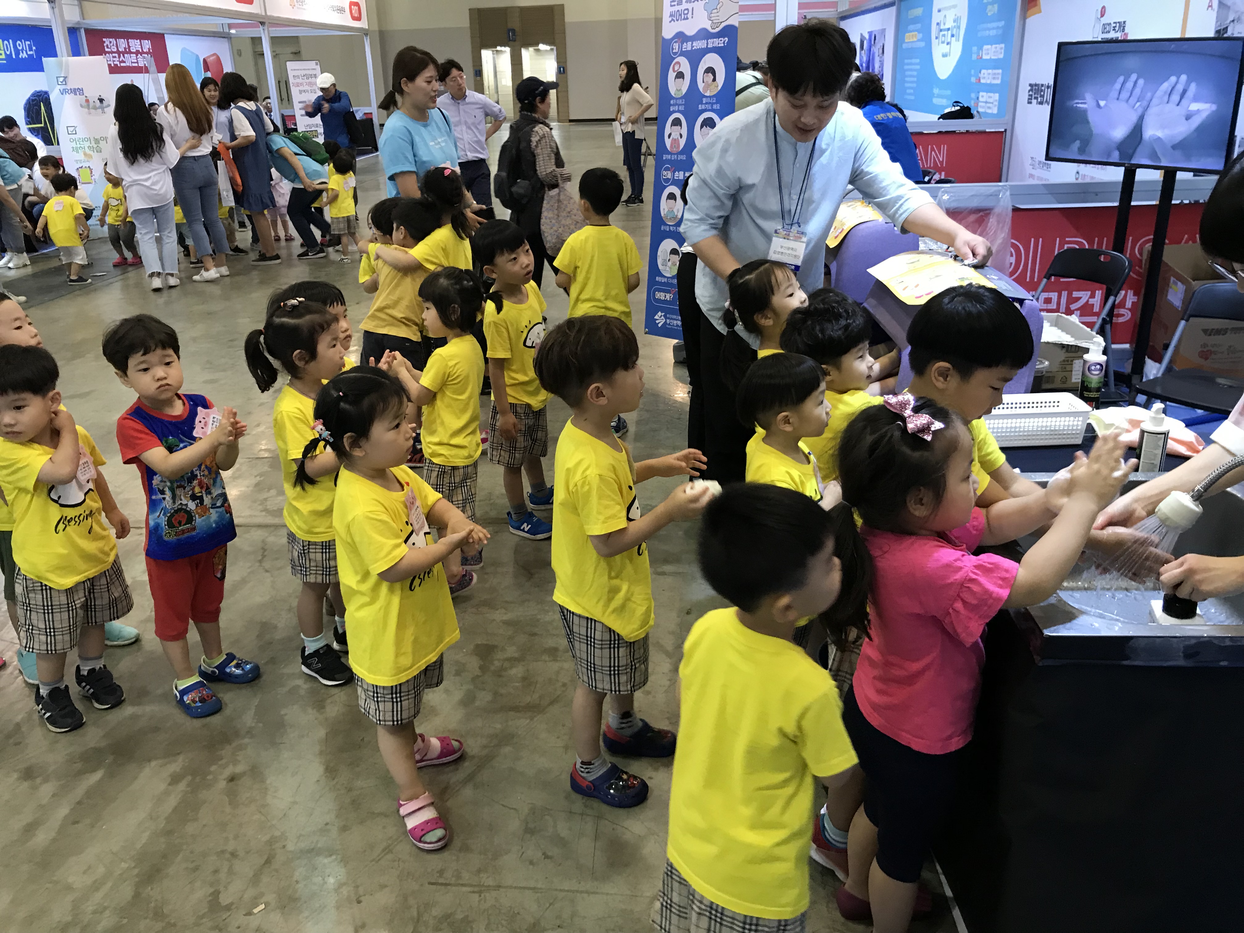 어린이들을 대상으로 손씻기 체험을 안내하고 있는 김승진 주임연구원과 노란색 티셔츠와 체크무늬 바지를 입고 차례를 기다리고 있는 어린이들의 모습 사진3